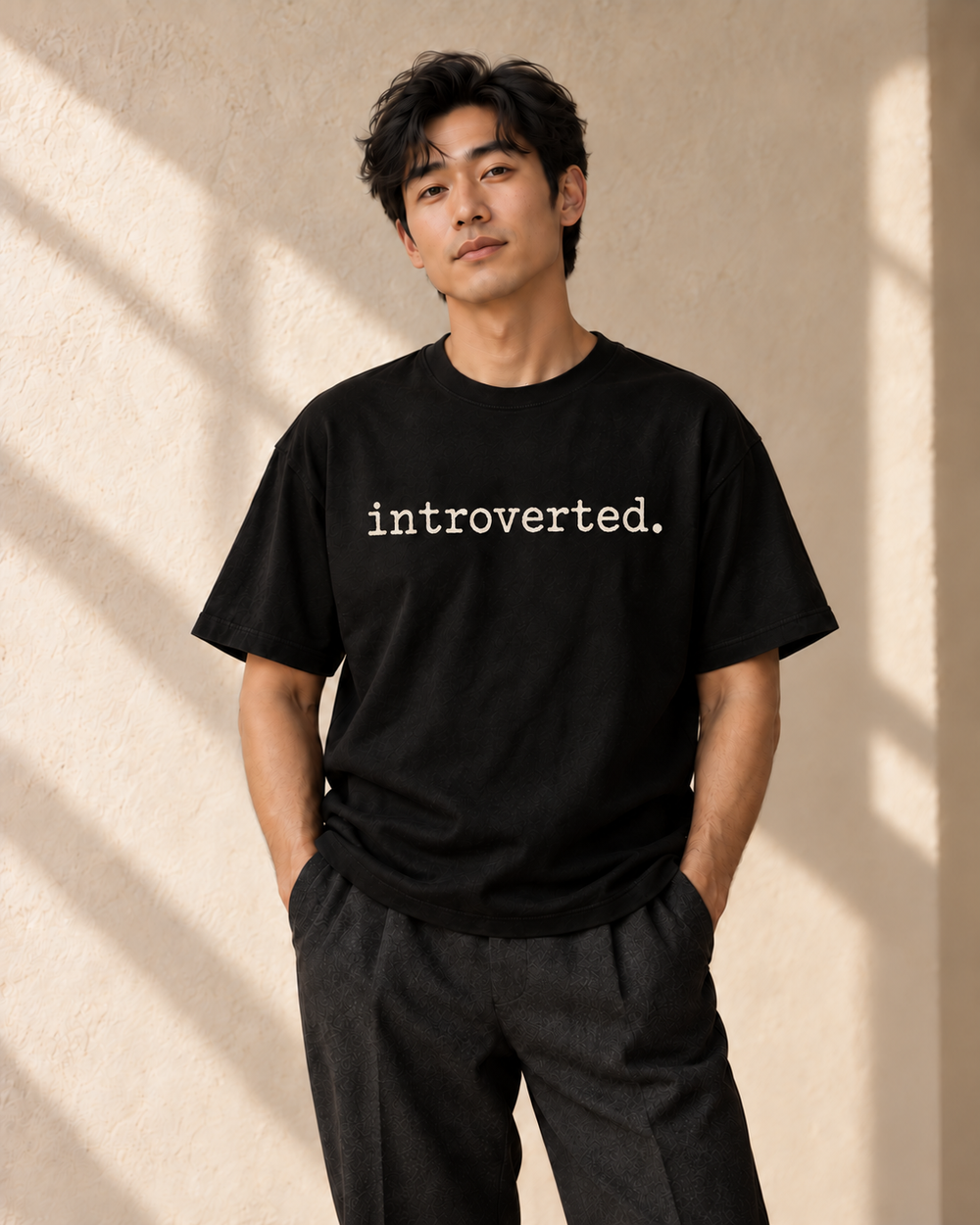 Concept image of an adult model wearing a black Adj tee reading introverted. in ivory lowercase textured typewriter lettering; not a physical product sample.