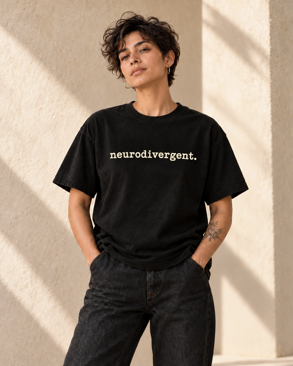 Concept image of an adult model wearing a black Adj tee reading neurodivergent. in ivory lowercase textured typewriter lettering; not a physical product sample.