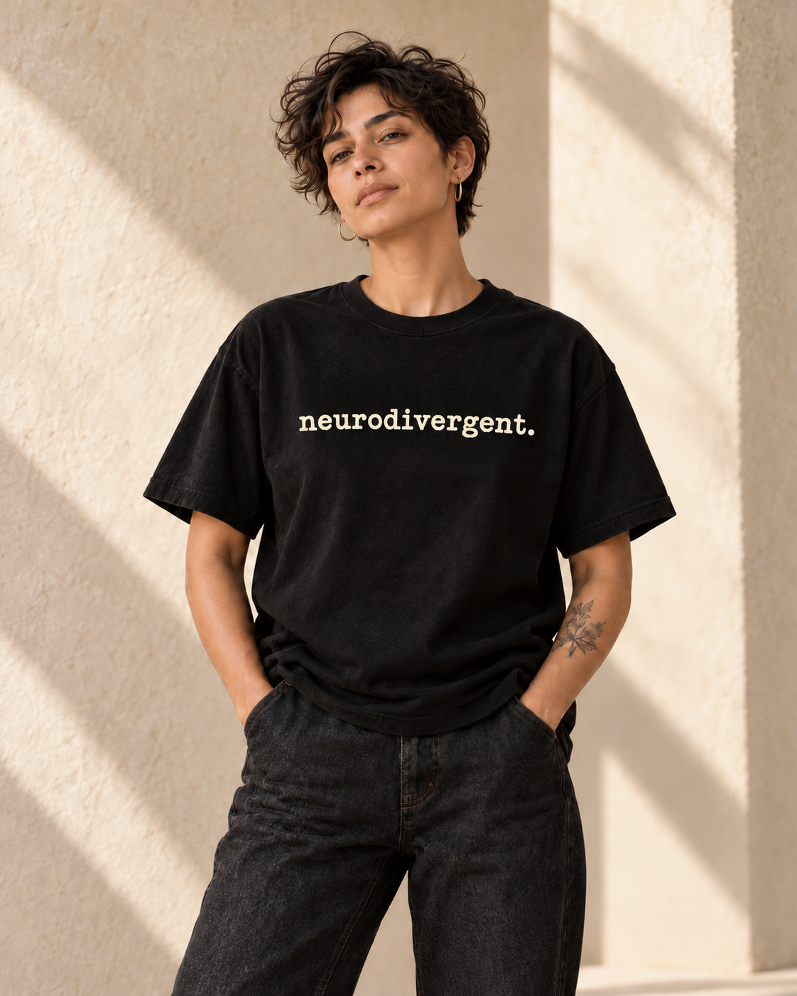 Concept image of an adult model wearing a black Adj tee reading neurodivergent. in ivory lowercase textured typewriter lettering; not a physical product sample.